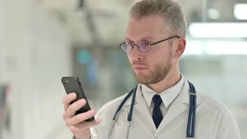 Doctor Looking at Mobile Phone in Hospital