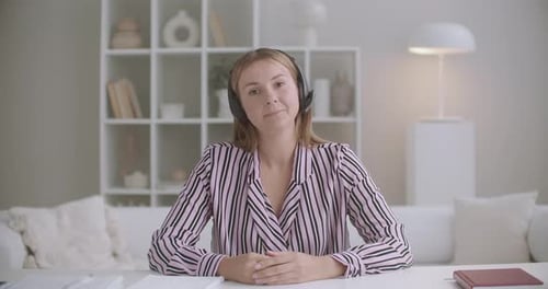 Jovem mulher amigável está ouvindo interlocutor por bate-papo por vídeo por fones de ouvido e balançando a cabeça olhando