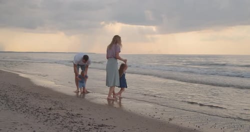 Young Parents Play with Their Children Near the Water at the Sea Coast