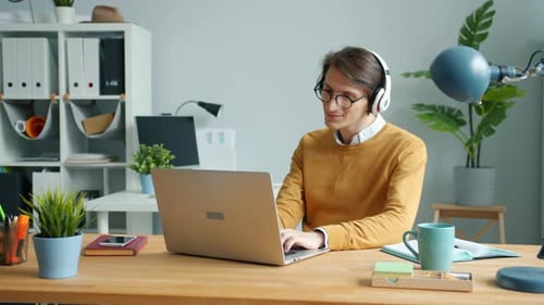 Handsome Guy Wearing Headphones Is Listening To Music in Modern Office at Work