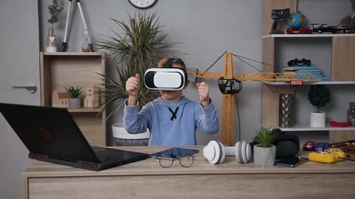5-7 Aged Boy Sitting at the Table in Child's Room and Using Virtual Reality Headset Plays Video Game