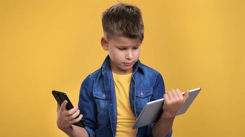 Modern Boy Child Use Smartphone and Tablet Pc Digital Display Technology Isolated on Orange Studio