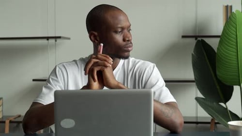 Thoughtful Black Businessman Sitting at a Desk with a Computer and Looking Away