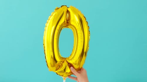 Festive Gold Zero Balloon Held Against Turquoise Background