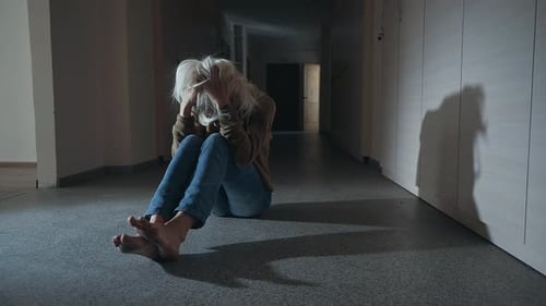 Distraught Woman Sitting on Floor in Dark Hallway