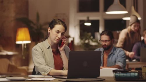 Woman Speaking on Phone and Working on Laptop in Office