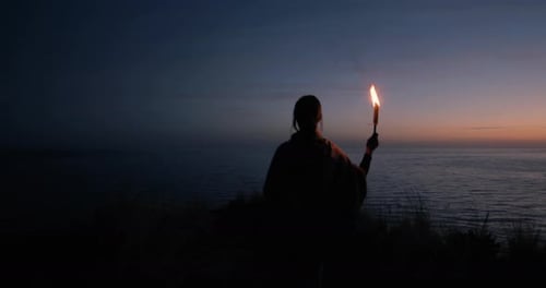Woman with Torch at Sunrise on Coastal Cliff
