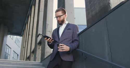 Office Manager in Business Clothes which Using His Mobile on the Steps of Business Center