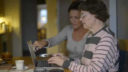 Woman Helping Senior with Laptop at Home