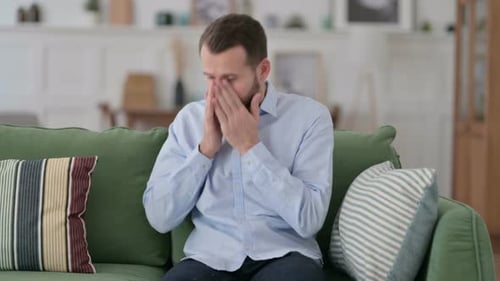 Sick Young Man Sneezing Sitting on Sofa