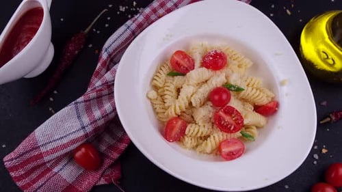 Drehbarer Teller mit Fuzulli-Nudeln von oben fallendem Parmesankäse mit Kirschtomaten auf einem schwarzen