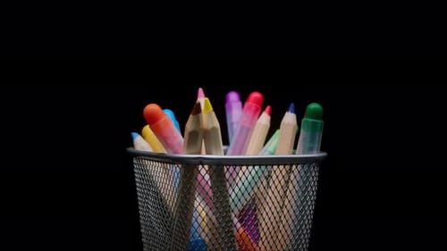 Closeup of Colored Pencils and Markers in a Metal Grey Basket Shooting Stationery on Black