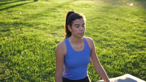 A fit young woman sitting in lotus position meditating in the park at sunrise to improve her mental