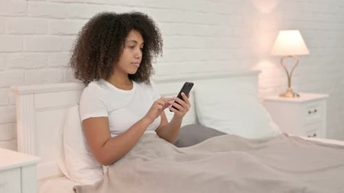 Young Adult Using a Smartphone in Bed at Home