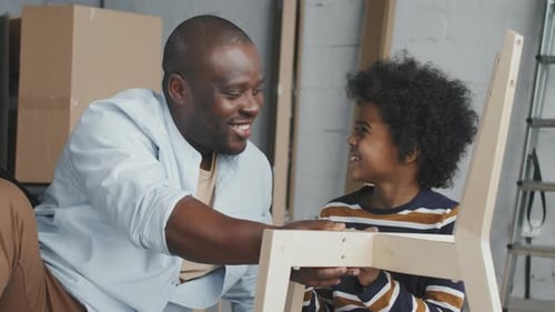 Happy African-American Father and Son Assembling Chair