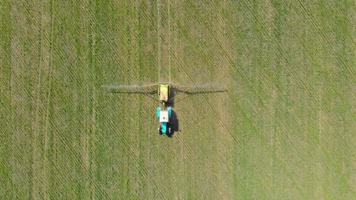 Aerial View of Farming Tractor Spraying on Field with Sprayer, Herbicides and Pesticides at Sunset