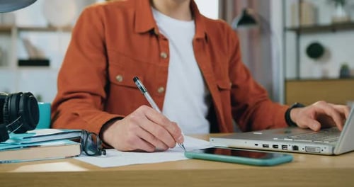 Person Writing and Typing at Desk