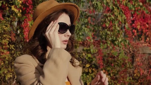 Elegant Woman Puts on Sunglasses in Autumn Setting