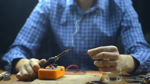 Male Engineer Solders Metal Wire During Working Day at Table in Service Center. Irrl