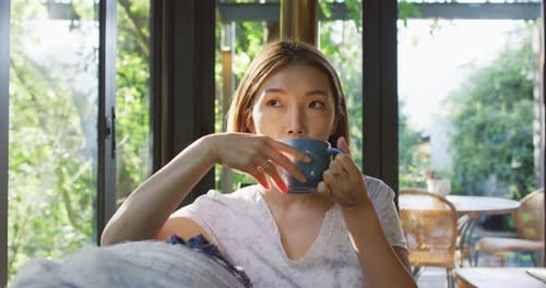 Asian woman drinking coffee and lying on couch