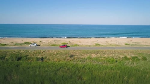 Drone Following Red Car Driving Along Peaceful Coastal Road with Scenic Blue Sea Horizon