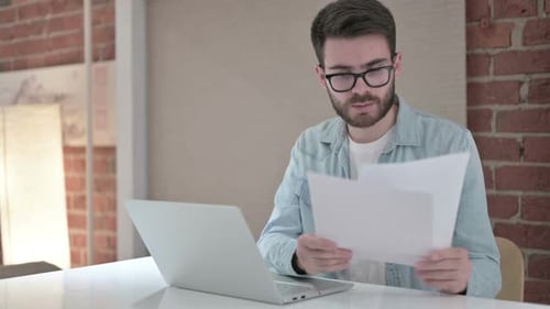 Young Male Designer Reading Documents and Working on Laptop