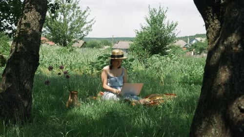 Woman with laptop computer in green garden in countryside