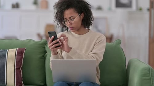 Woman Uses Phone and Laptop at Home on Couch