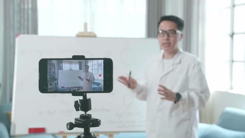 Close Up Of Smartphone Camera Recording Asian Male Teacher With Glasses Teaching Chemist At Home