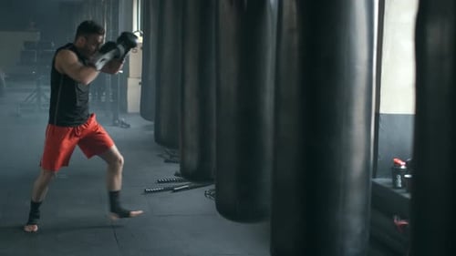 Man Punches and Kicks Heavy Bag in Gym