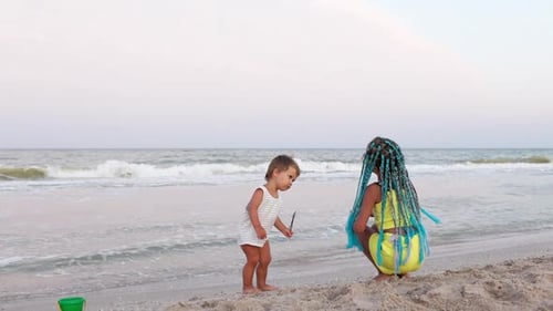 A Boy in a Striped Tshirt is Dancing to the Music with His Sister African Braids on the Beach Near