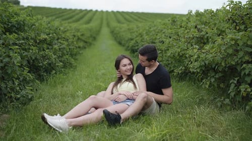 Young Couple Resting in Embraces and Kisses Among Currant Plantation