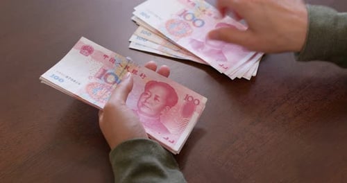 Hands Counting Chinese Yuan on Wooden Table