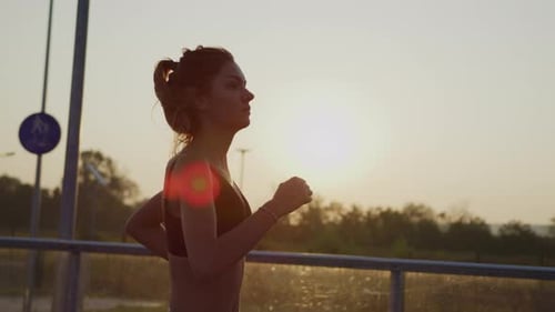 Young Woman Jogging on Bridge During Sunset
