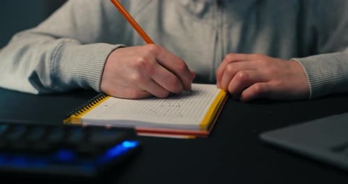 A Boy Sits in Room in the Evening in Front of Computer Screen and Laptop Working on a School Project