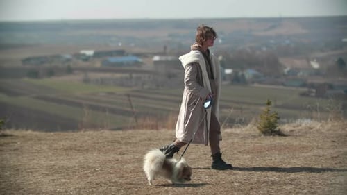 A Young Teenager Girl is Walking with a Small White Pomeranian Spitz on the Hill