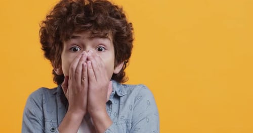 Studio Portrait of Amazed Little Boy Closing Mouth in Fear, Looking Frightened
