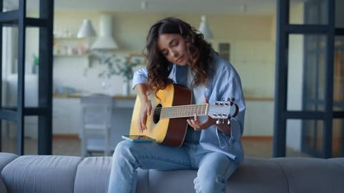 Woman Plays Guitar on Couch in Living Room
