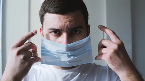 Man Puts on Blue Medical Face Mask
