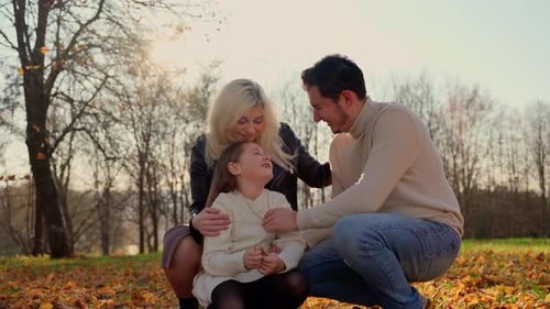 Happy family portrait at autumn park outdoors. Three persons father mother and child girl sitting