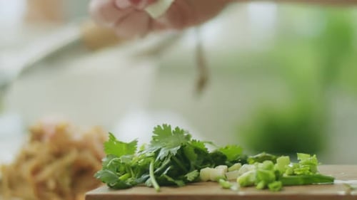 Woman adding greens on portion of wok noodles