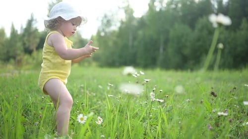 Little Funny Cute Blonde Girl Child Toddler in Yellow Bodysuit and White Hat Walking in Field with