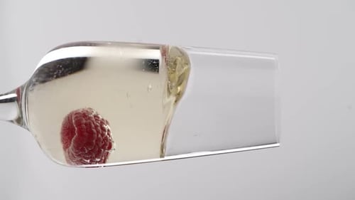 Vidéo verticale, gros plan : des fraises tombent dans une coupe de champagne