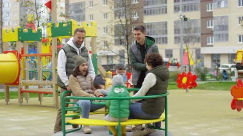 Young Families Having Fun on Merry-Go-Round at Playground