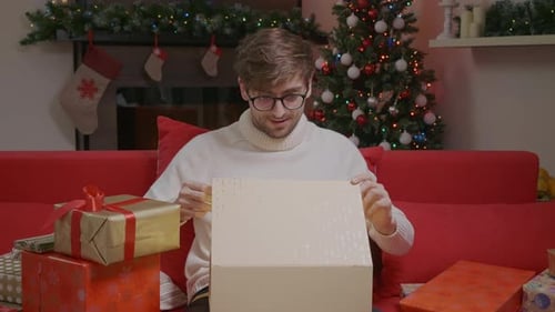 Young Adult Opens Christmas Gift on Couch