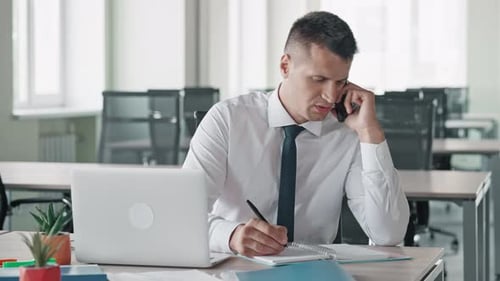 Man Talking on Phone and Writing in Office