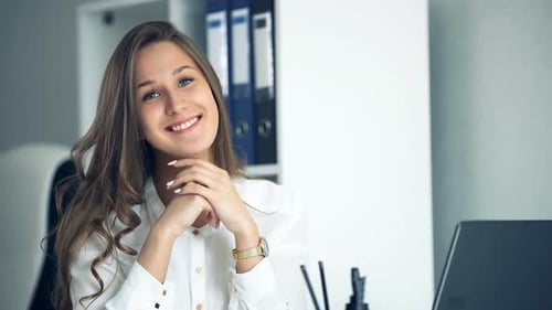 Cheerful Businesswoman Sitting at the Table in Office and Looking at Camera