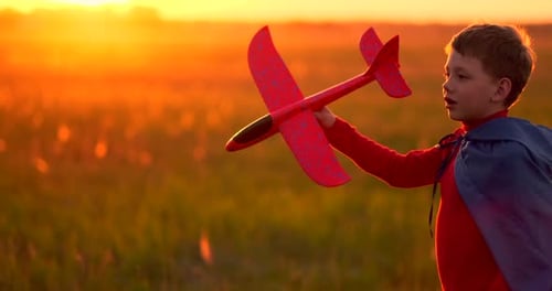 The Boy Runs Across the Field with a Plane in His Hands at Sunset