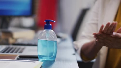 Mid section of woman sanitizing her hands at office