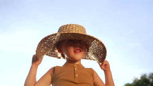Smiling Child Playing with Straw Hat Outdoors